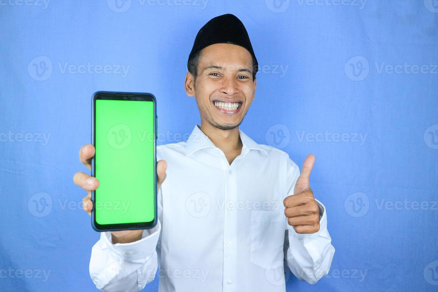 Smiling happy of muslim asian man wearing cap showing empty phone screen. Advertising concept photo