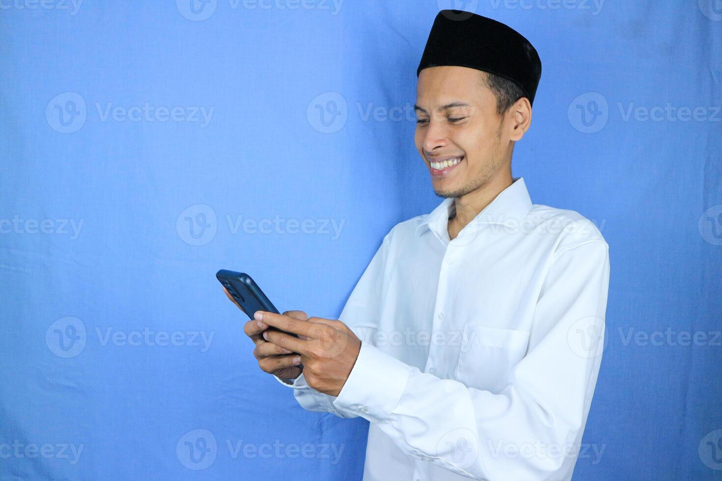 Smiling happy of muslim asian man wearing cap reading message on mobile phone photo