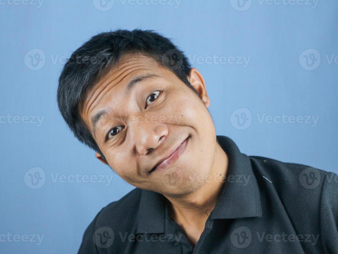 funny face expression of young asian man smiling looking at camera, isolated on blue background. photo