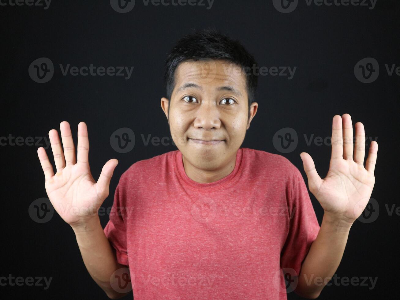 Asian man in red tshirt showed no idea gesture, shrugged and raised his hand. isolated on black photo