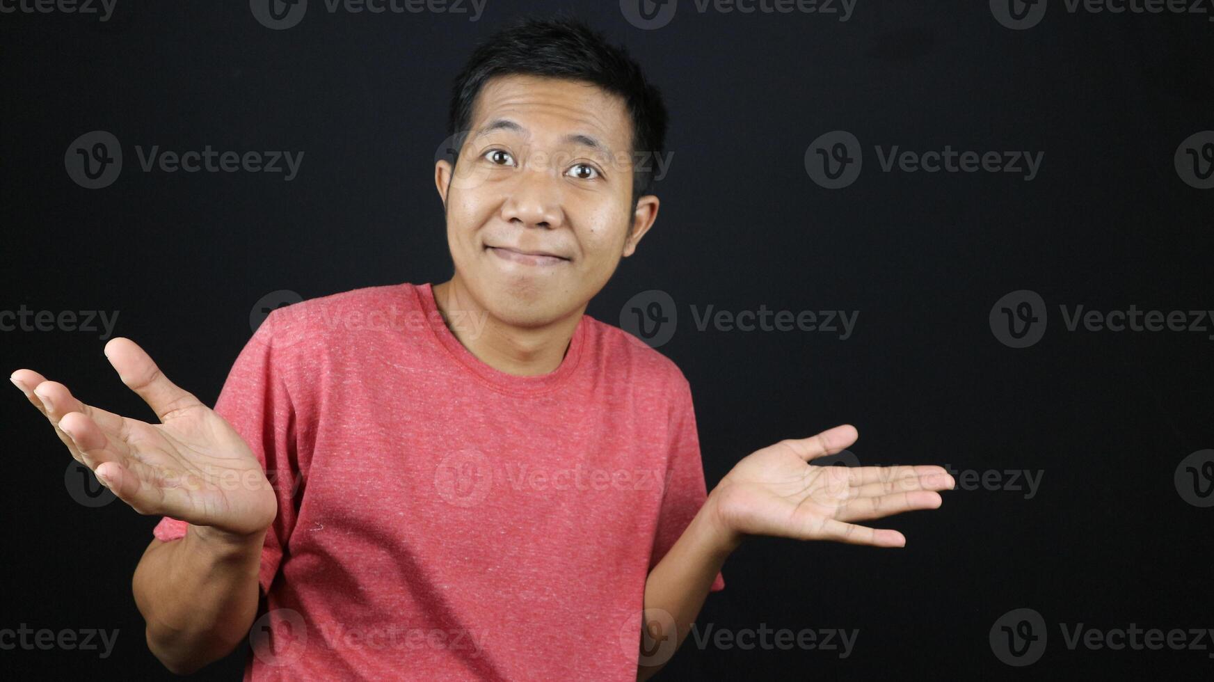 Asian man in red tshirt showed no idea gesture, shrugged and raised his hand. isolated on black photo