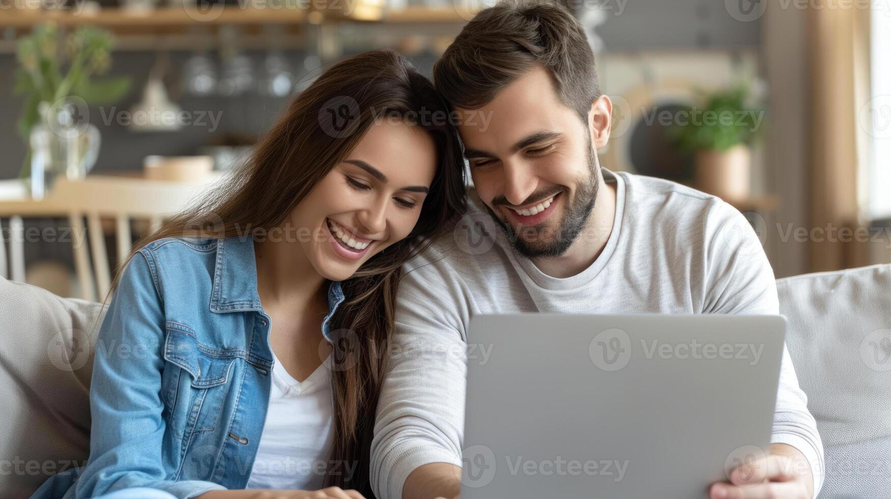 A man and woman are seated on a couch, engaged in viewing content on a laptop together photo
