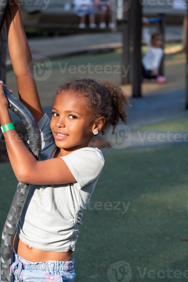 A smiling African American girl with curly hair climbs on playground equipment, capturing active play and enjoyment on a sunny day. photo