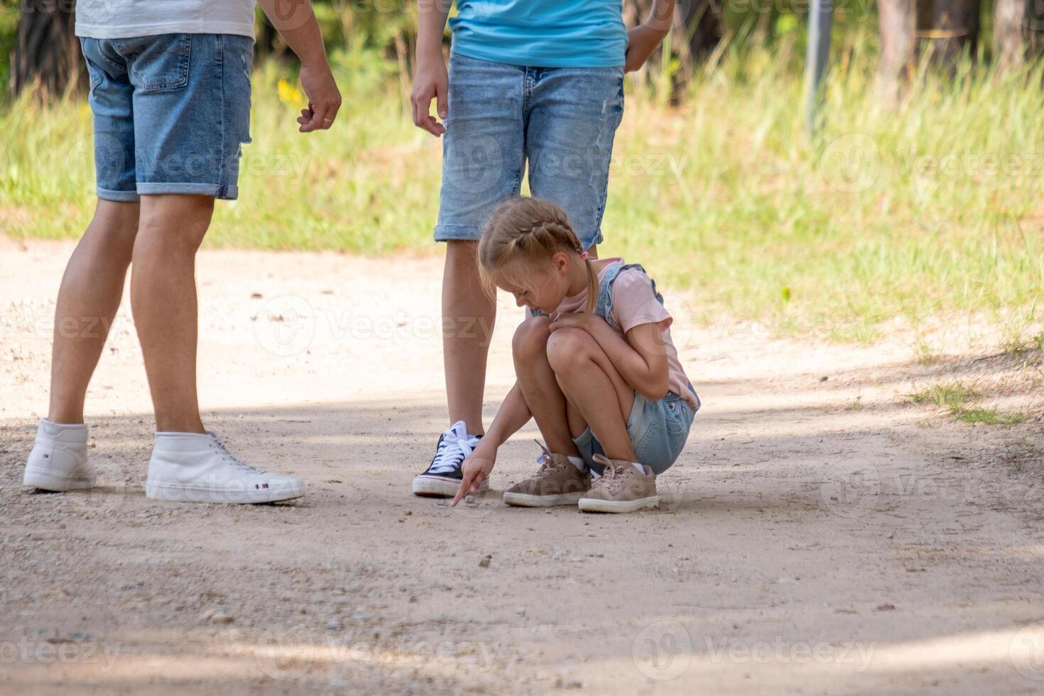 A little girl crouched on the ground looking at rocks with her family standing around her. A original play with nature materials. photo