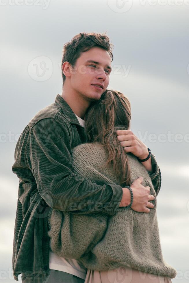 Man hugging a woman on the beach, gazing into the distance. Captures a moment of contemplation within a romantic setting. photo