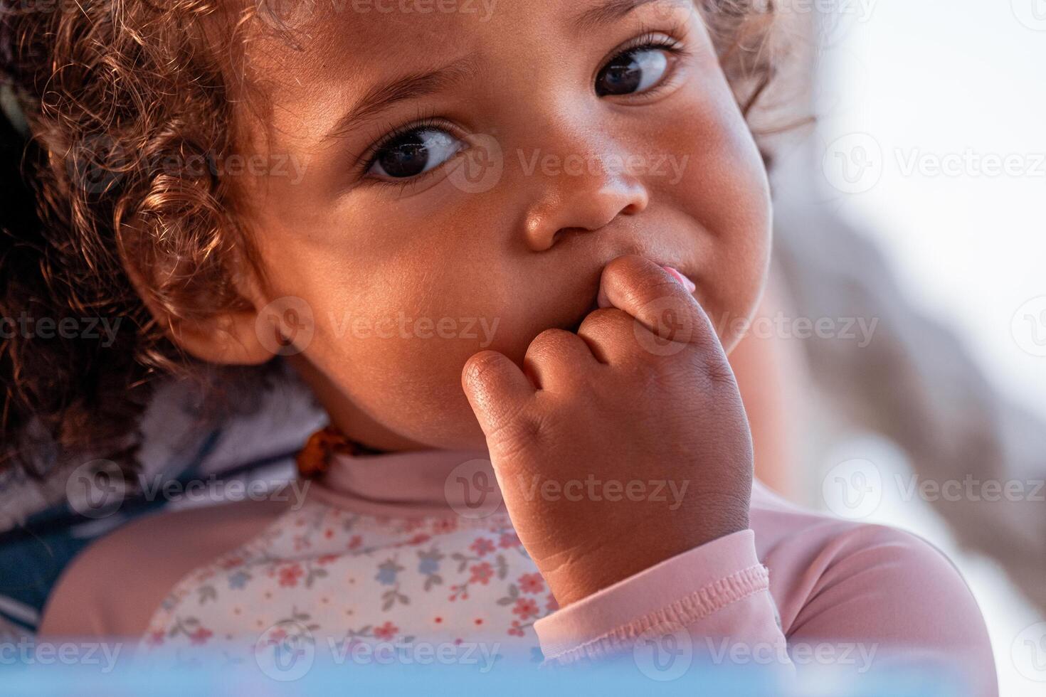 A pensive toddler with curly hair, finger on lips, gazes thoughtfully. expression suggests contemplation or worry, fitting for themes of childhood introspection or early stress. photo