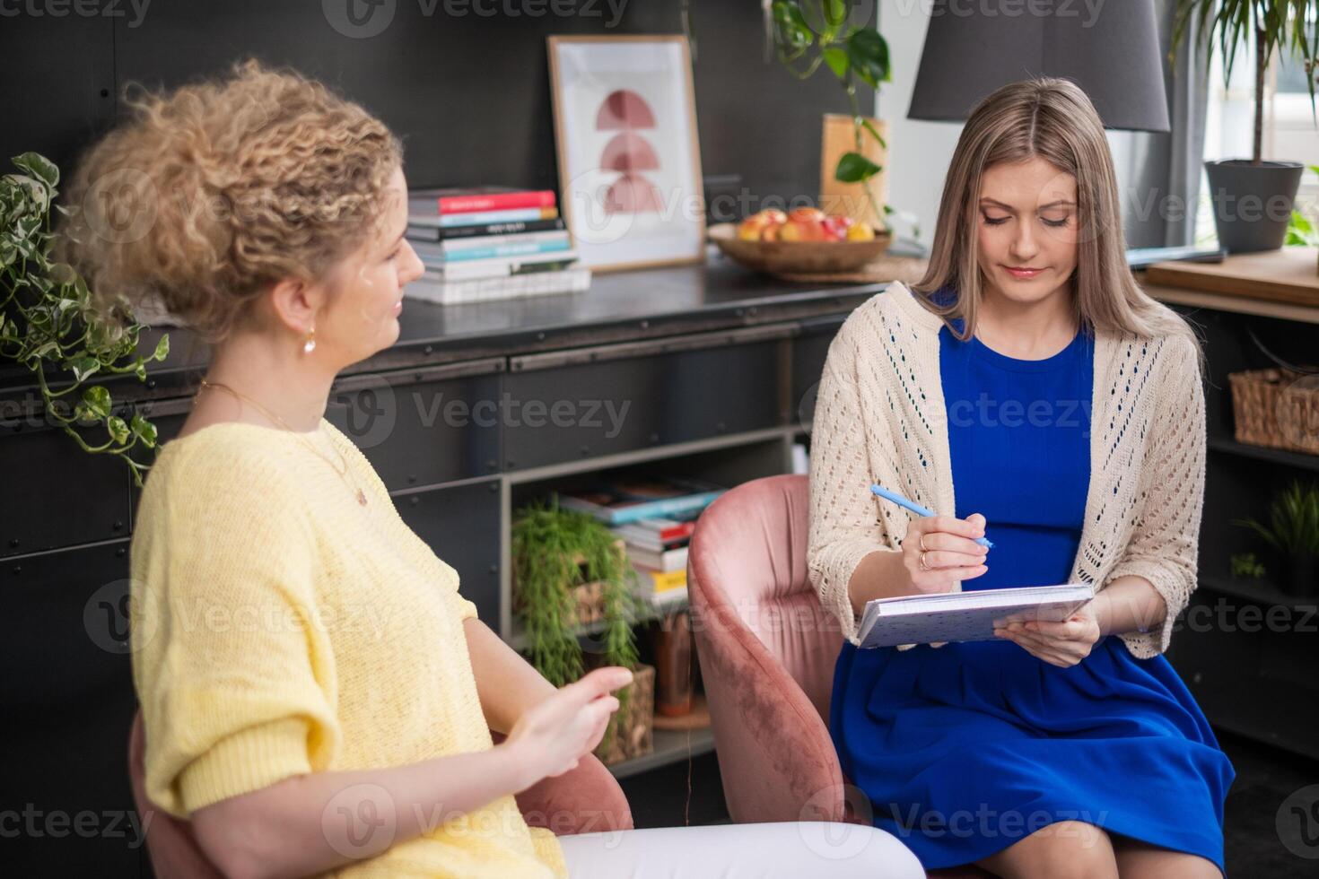 A coaching Mentor in yellow sweater guiding client, pen in hand, in a supportive psychotherapy environment, business and self growth session. photo