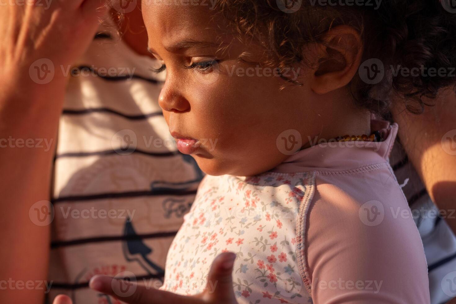 With soft curls framing a contemplative expression, this small child sucking on a thumb appears lost in thought, evoking themes of youth and reflection. photo