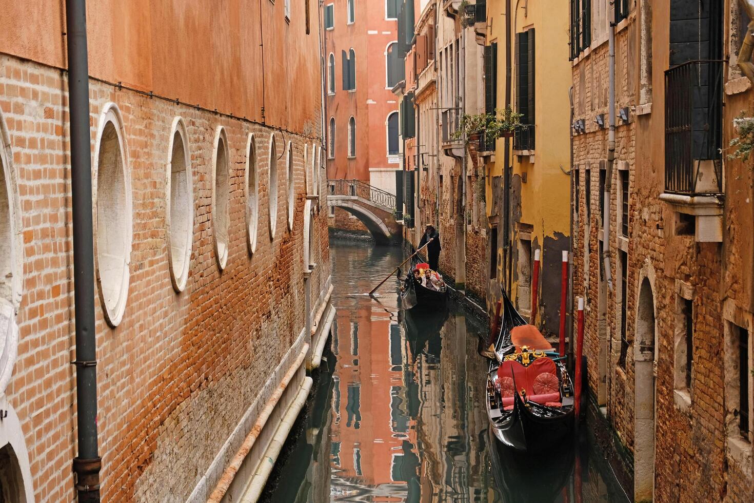 An empty gondola is parked in a Venetian canal. View of the bridge over the canal, reflection of the bridge in the water. Typical narrow street with historical houses in Venice. photo