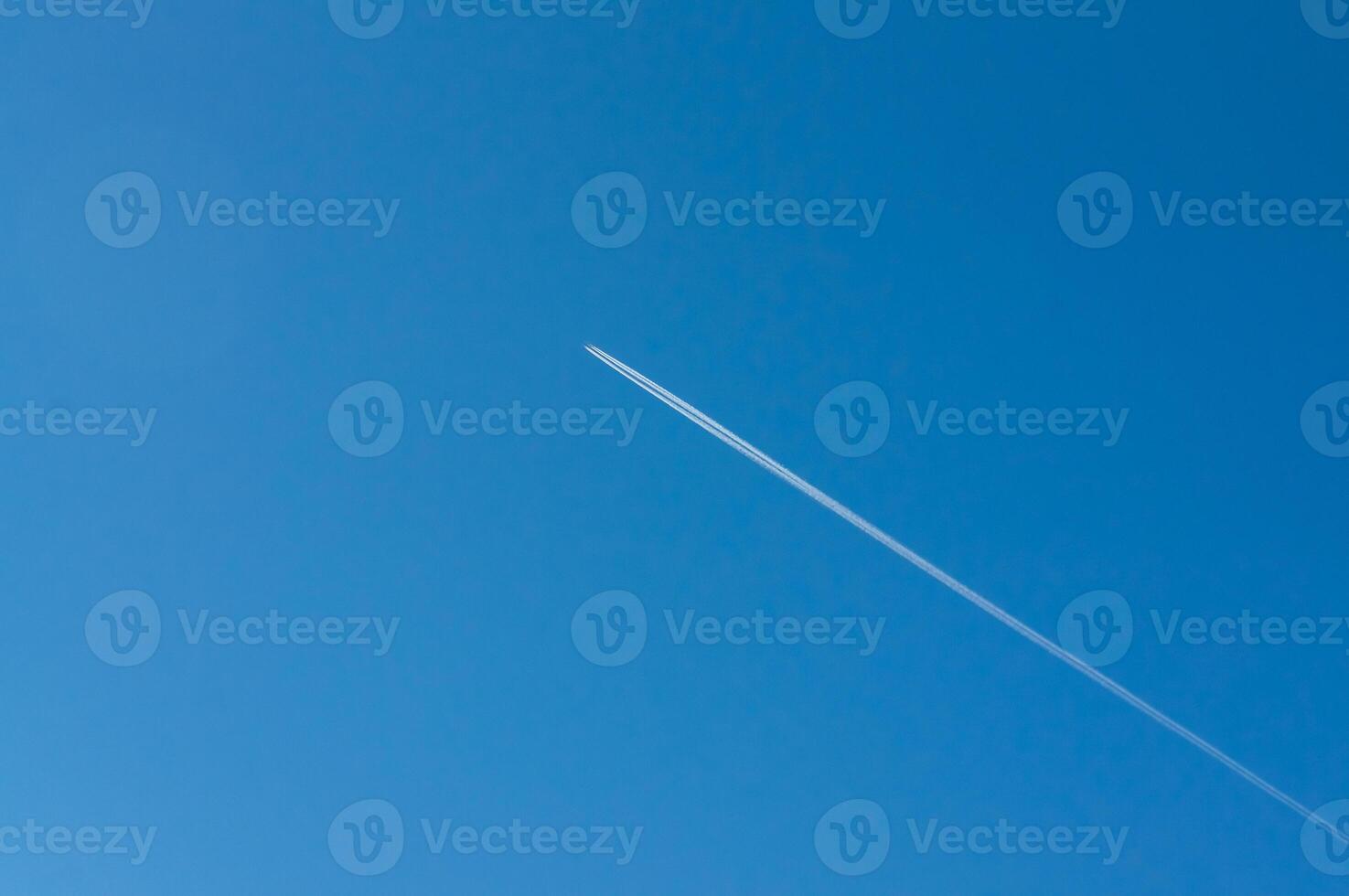 Against the serene blue sky, a jet streaks, its contrail a fleeting mark of human passage, connecting distant places and leaving a temporary imprint on the vastness of the atmosphere. photo
