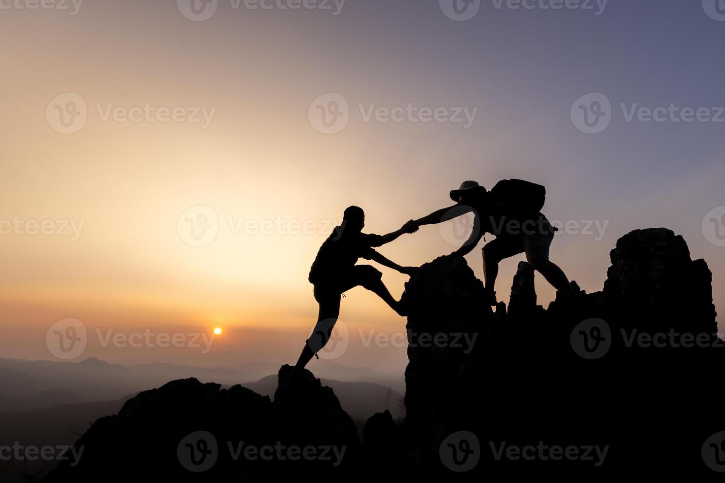Silhouette of person hikers climbing up mountain cliff and one of them giving helping hand. People helping and, team work concept. photo