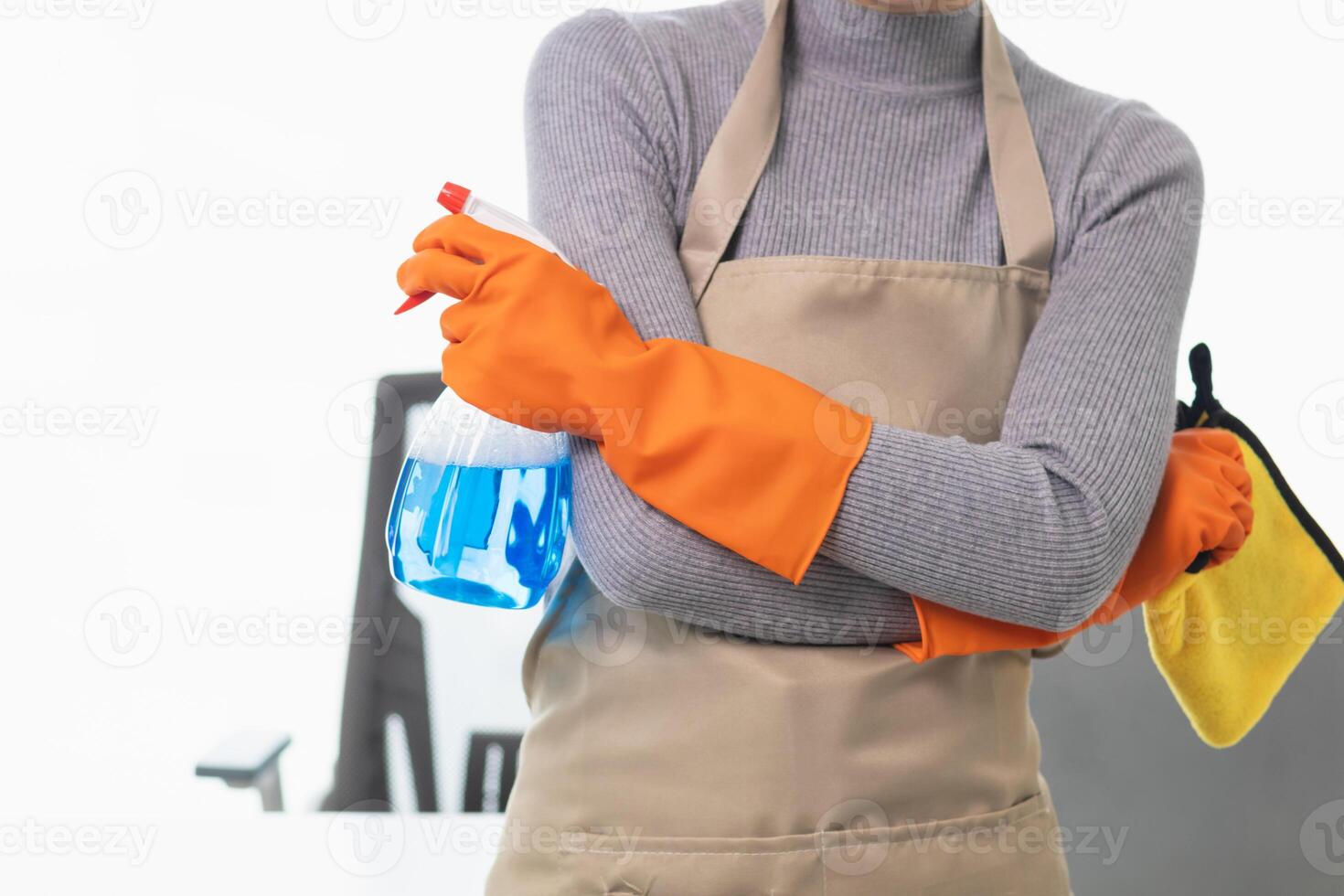 young woman puts on an apron and rubber gloves before holding spray bottle filled with cleaner and disinfectant to use to clean furniture surfaces clean and germ free. Concept of contract Hire cleaner photo