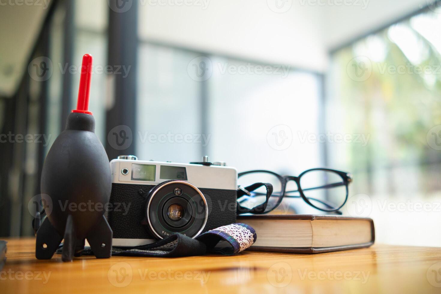 A vintage film camera sits on a table in an office and a book stands out in the background. A vintage film camera with a simple design sits on a table in an office and has copy space for text. photo