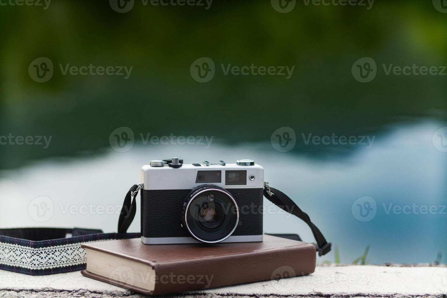 A vintage film camera sits on a table in an office and a book stands out in the background. A vintage film camera with a simple design sits on a table in an office and has copy space for text. photo