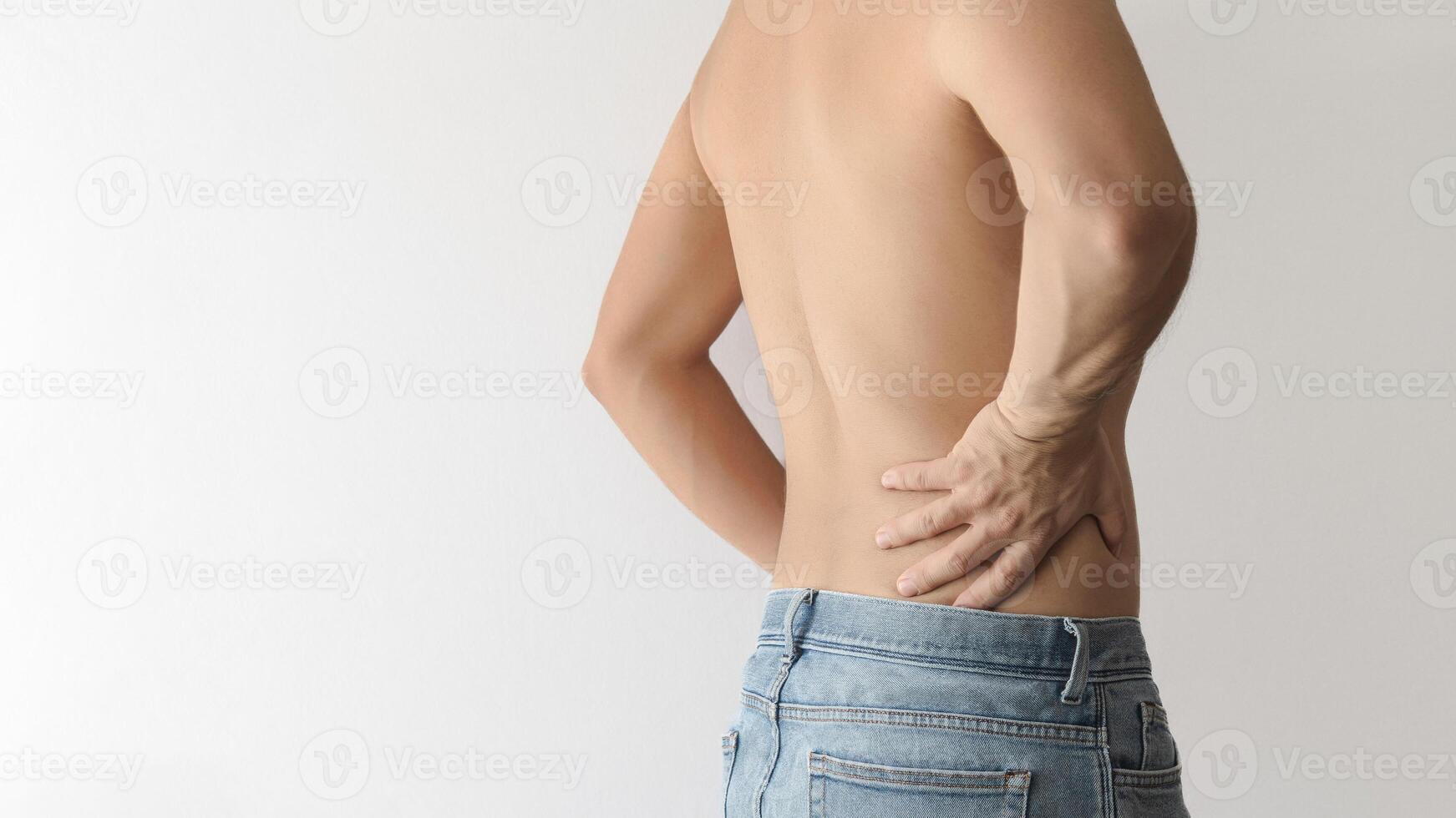 Shirtless man turning his back and touching his lower back with his hand due to pain, white background with space for text on the left photo