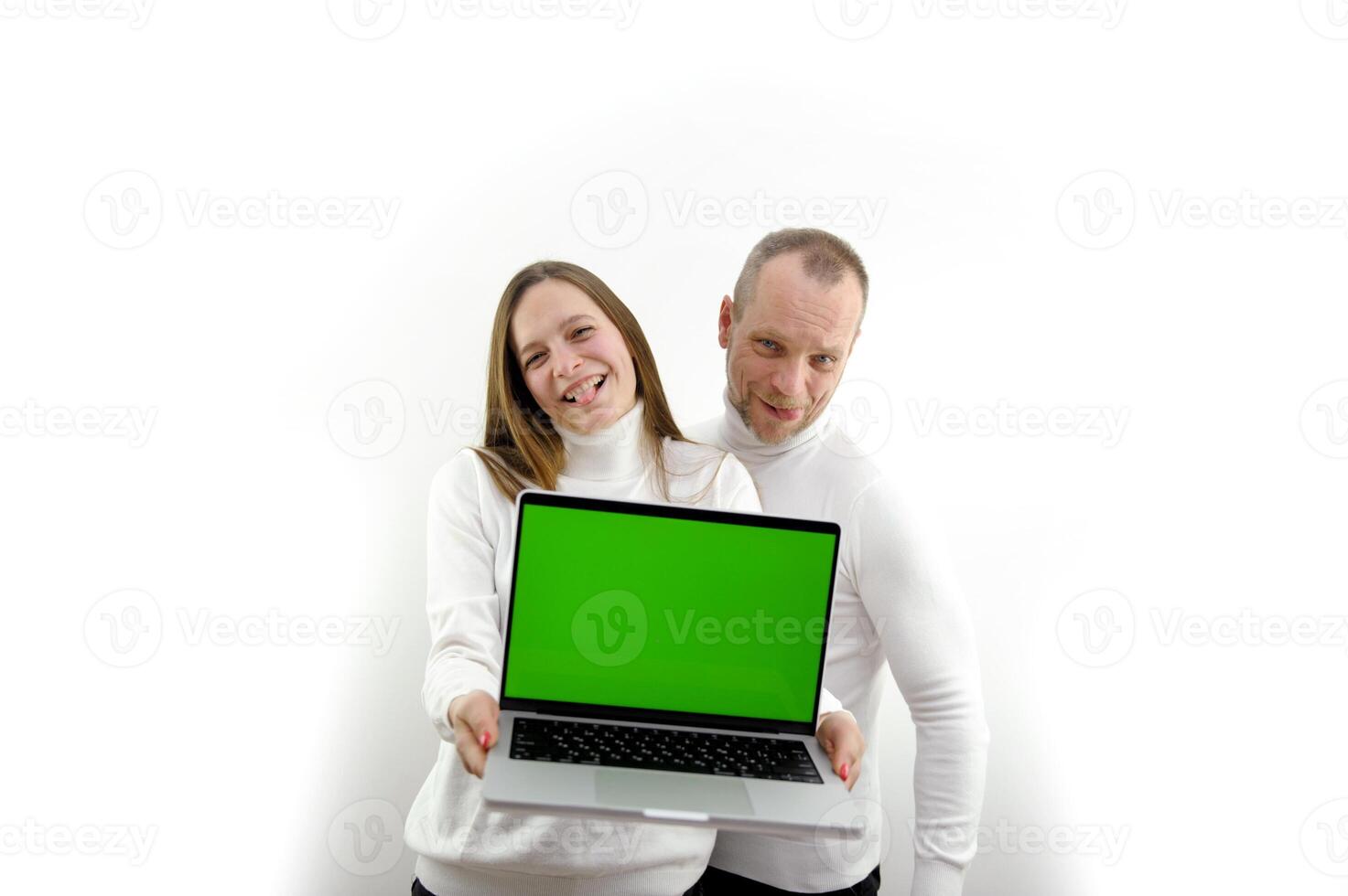 father and adult daughter show laptop with blank screen space for text girl shows tongue smiling fun joy joke white background white clothes Silver laptop chroma key green screen photo