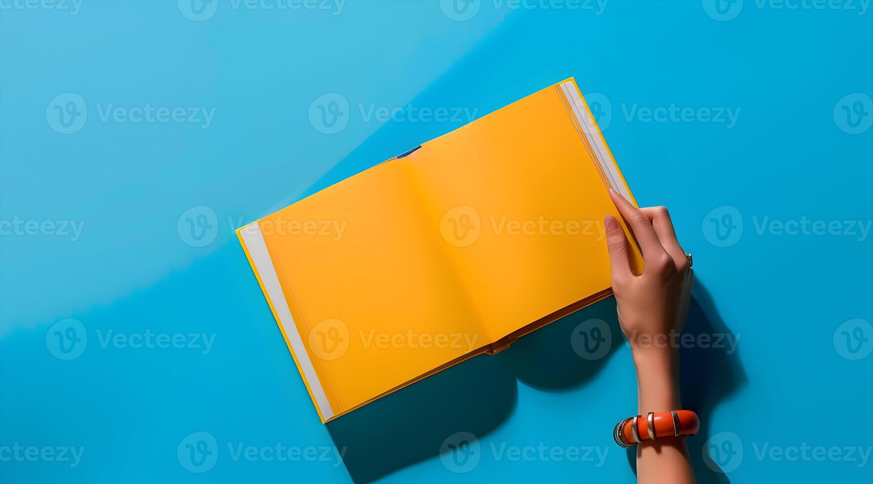 Book mock up with a hand isolated on a blue background. A hand holding an open yellow magazine with yellow empty page. photo