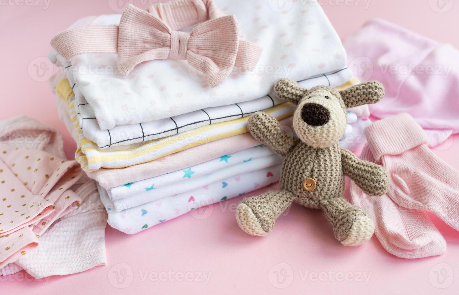 Baby crocketed toy of dog next to a stack rompers for kids photo