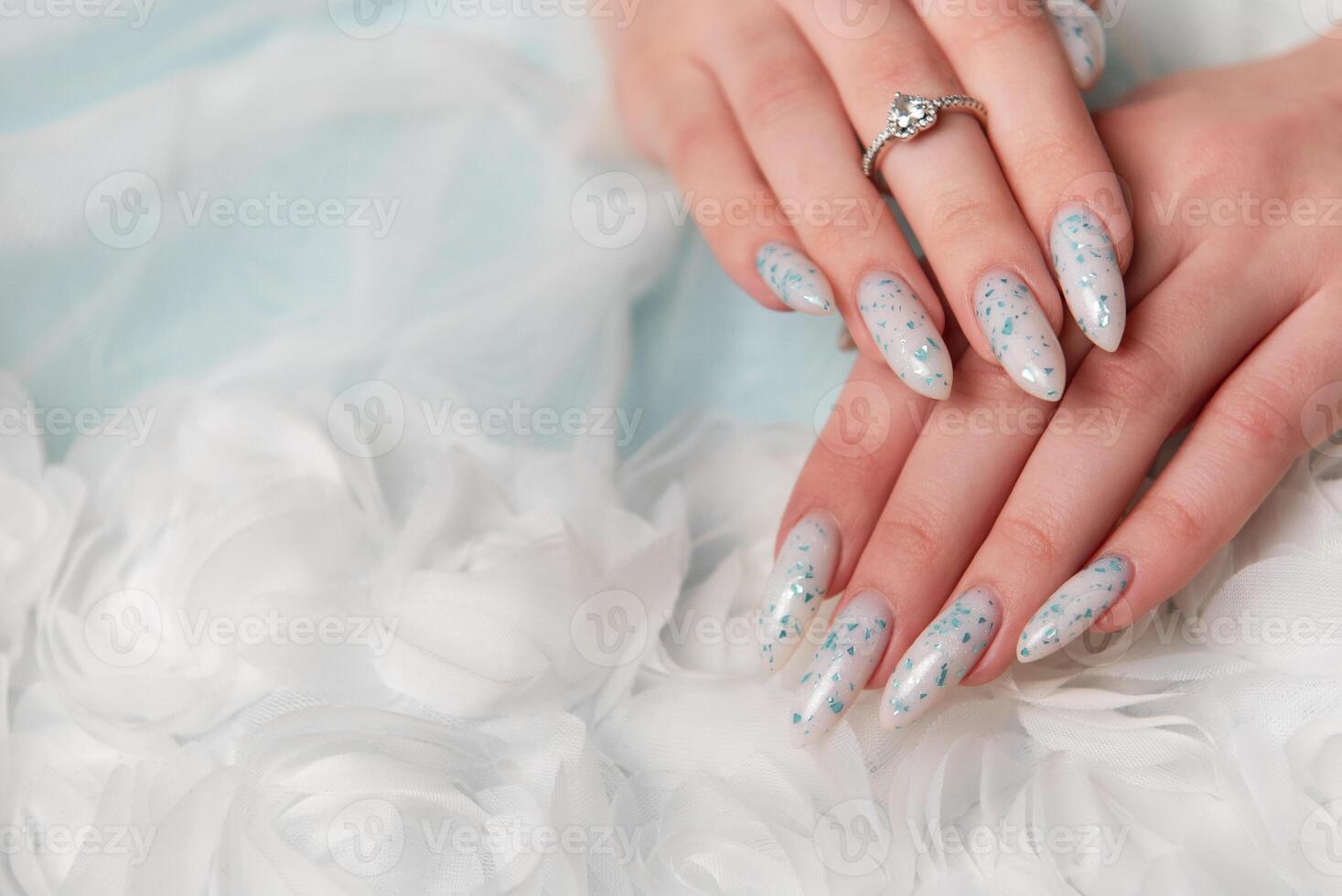 Elegant Hands Featuring Sparkling Ring and Blue Floral Manicure on Delicate White Fabric photo