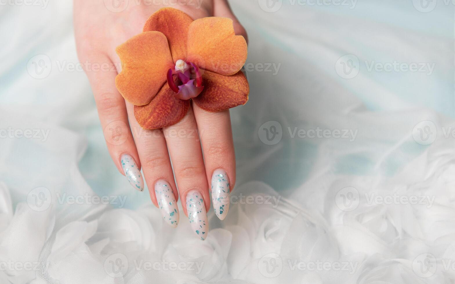 Showcasing Floral Nail Art and Holding an Orange Blossom on a Soft Textured Surface photo