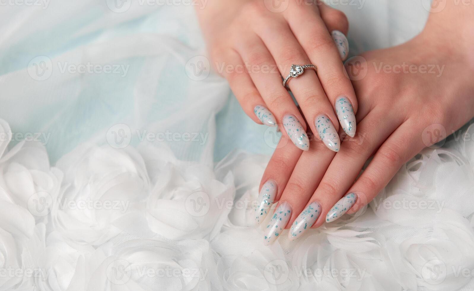 Elegant Hands Featuring Sparkling Ring and Blue Floral Manicure on Delicate White Fabric photo