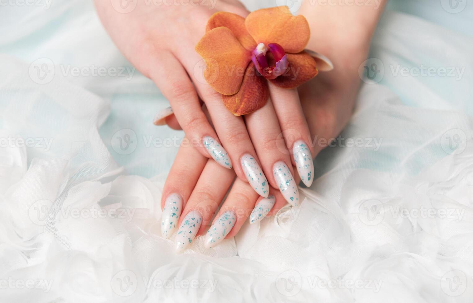 Showcasing Floral Nail Art and Holding an Orange Blossom on a Soft Textured Surface photo
