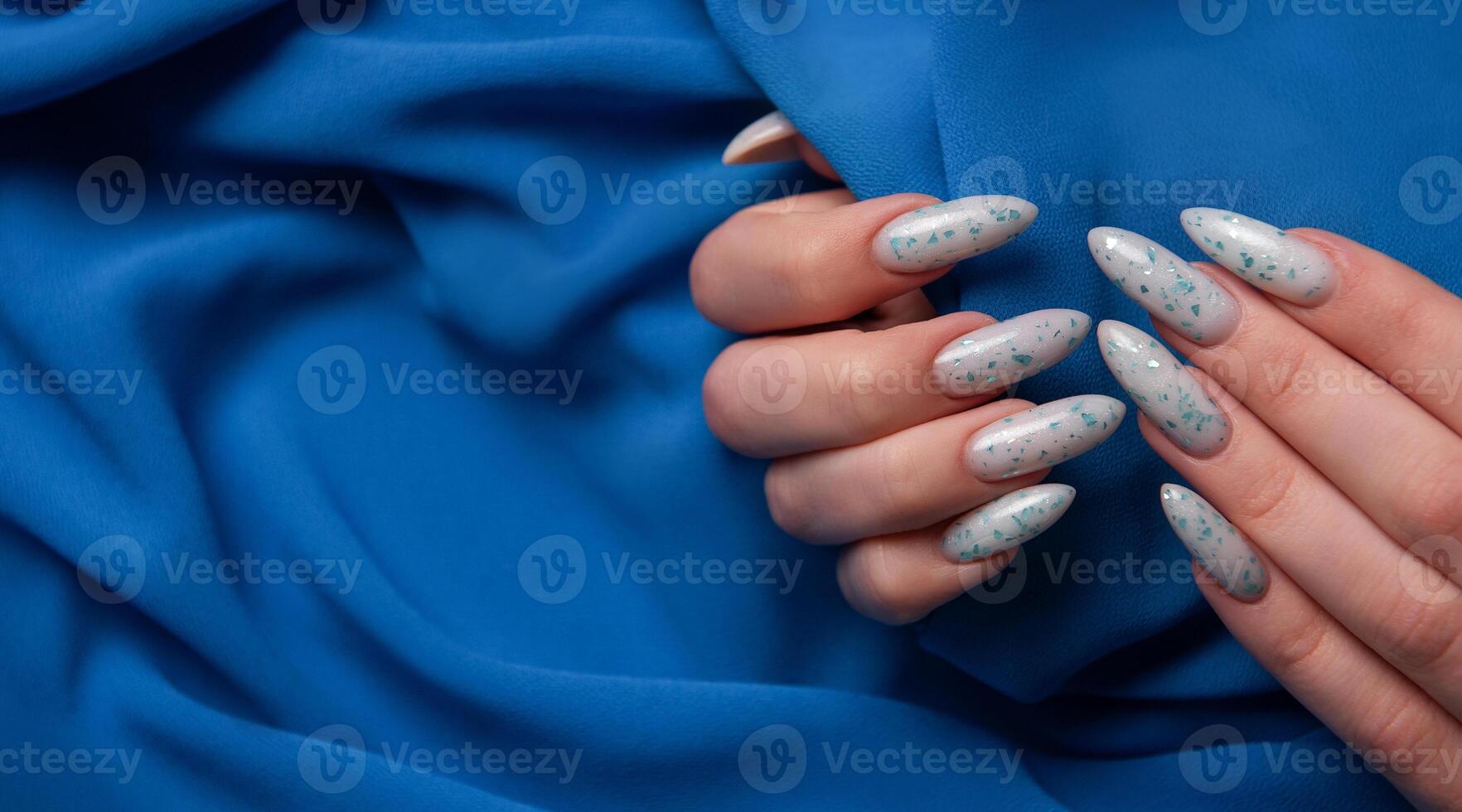 Female hands with blue nail design on blue textile background. photo