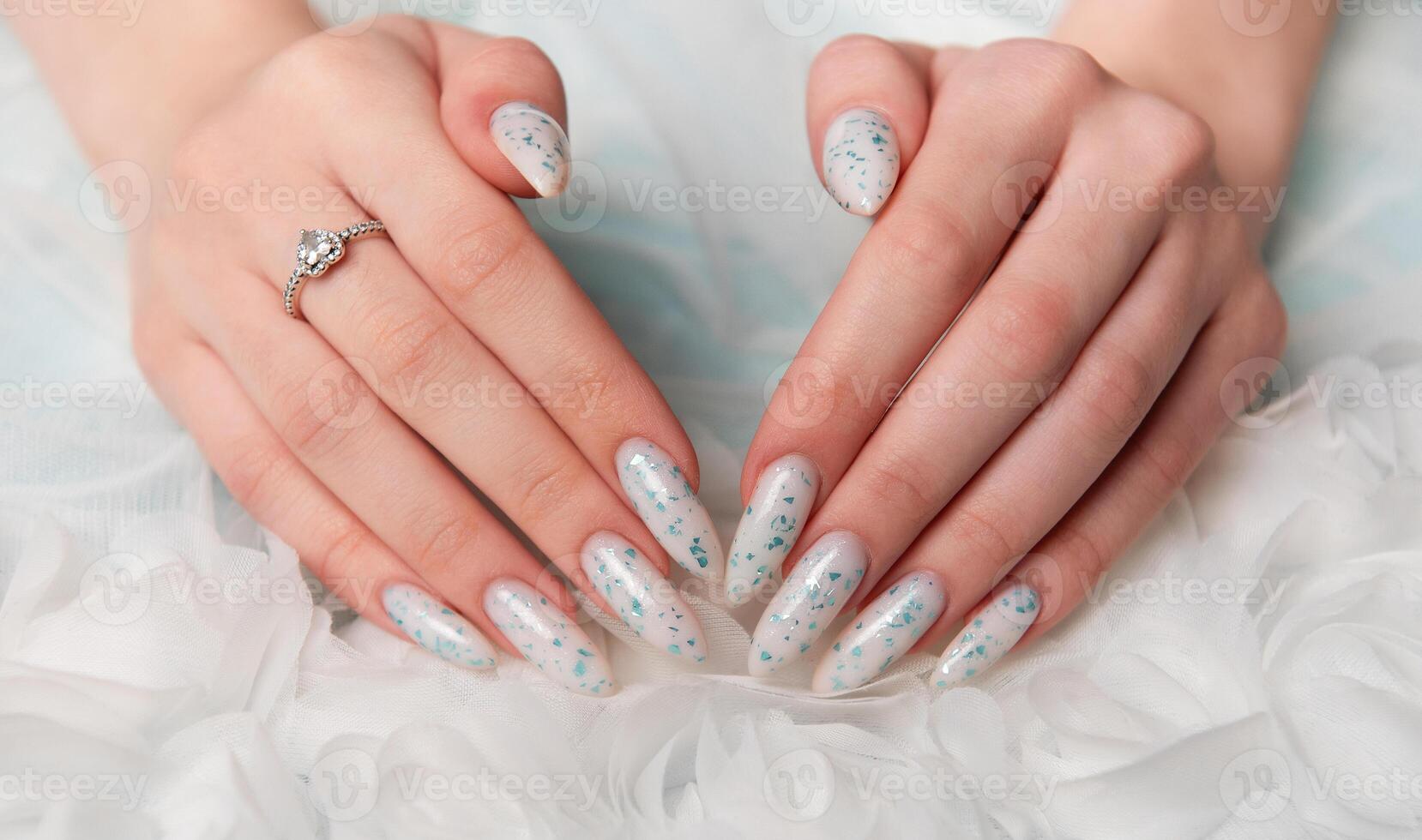 Elegant Hands Featuring Sparkling Ring and Blue Floral Manicure on Delicate White Fabric photo