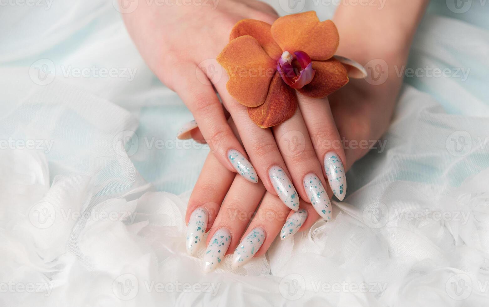 Showcasing Floral Nail Art and Holding an Orange Blossom on a Soft Textured Surface photo