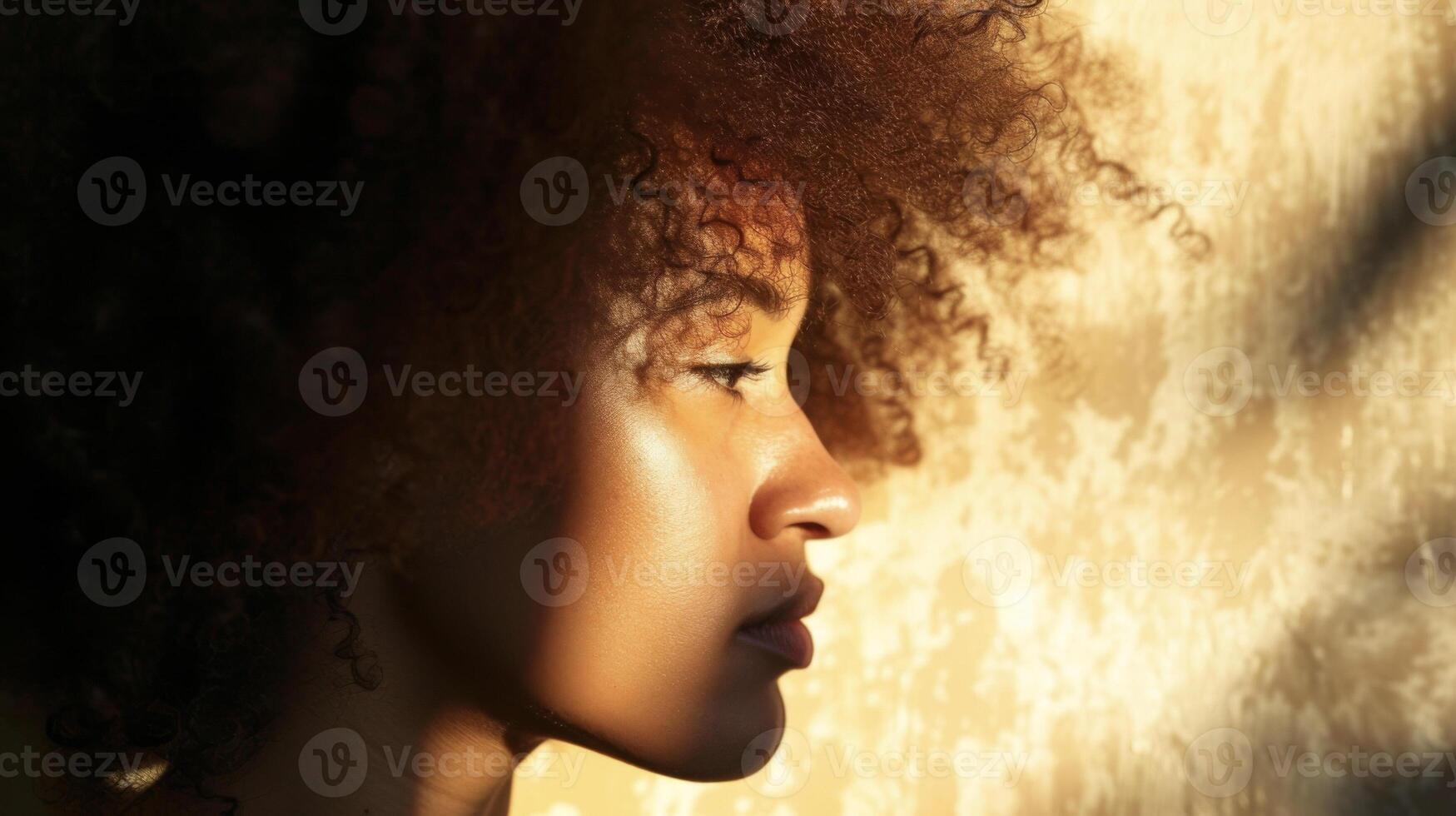 A womans profile with light shining through her curly hair casting a bold and dramatic shadow on the wall behind her photo