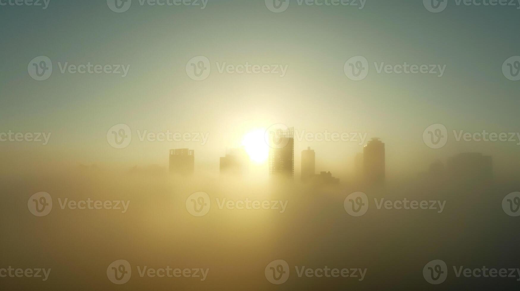 The hazy outline of a city skyline obscured by dense fog with the sun peeking through in the background photo
