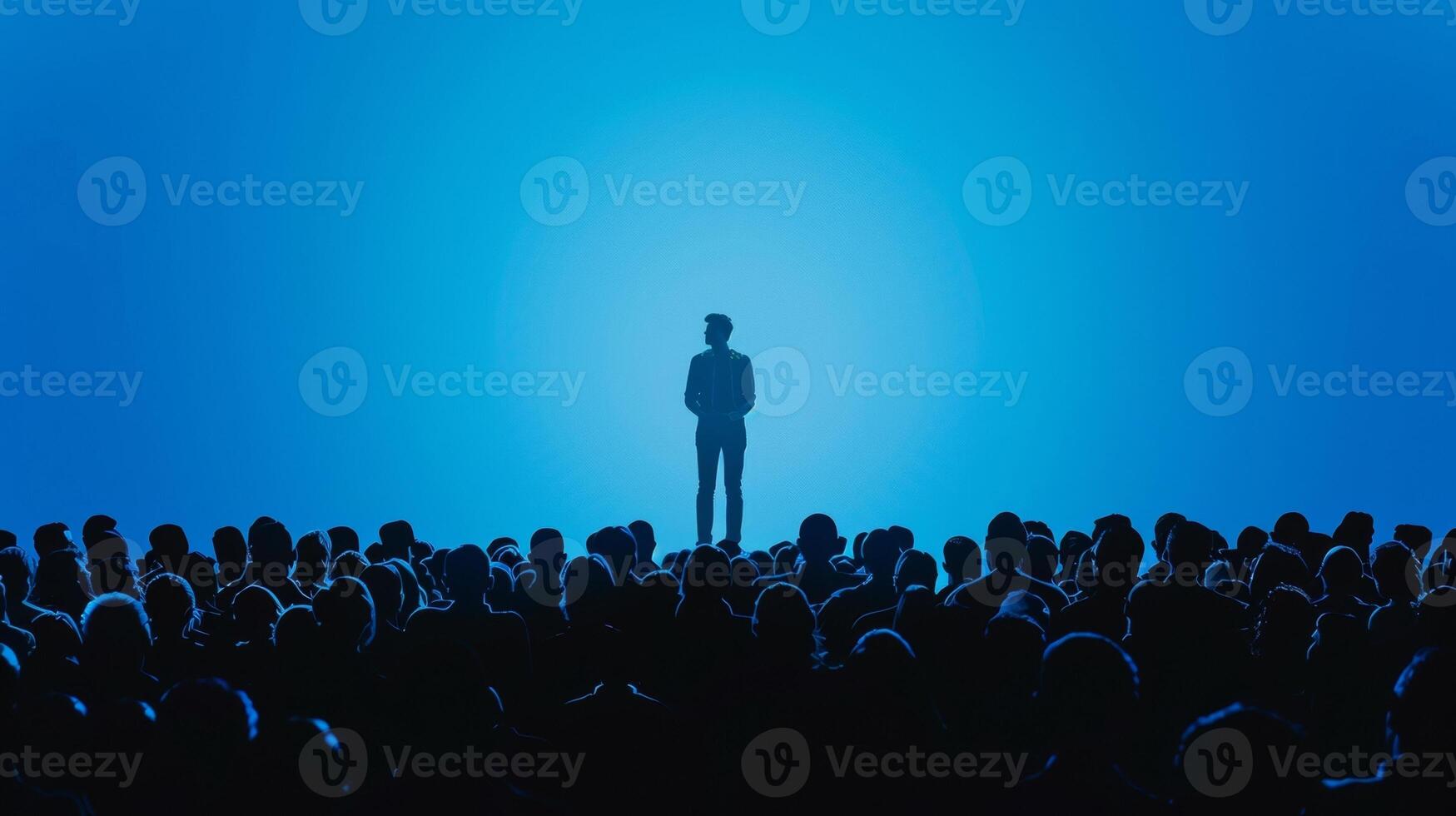A silhouette of a person standing on a stage surrounded by a sea of audience members. This skilled negotiator has captured the attention of the entire room as they deliver a persuasive photo