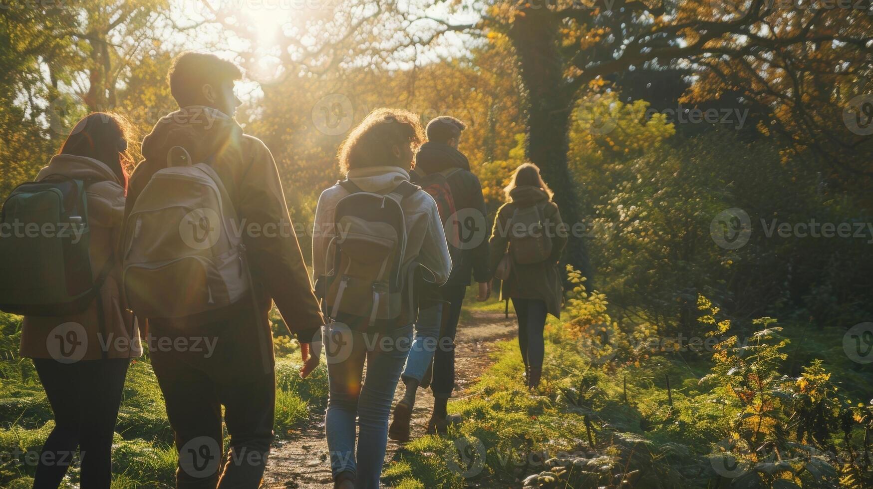 A group of friends walk away from the camera chatting and laughing as they make way through the tranquil green space. The sun . photo