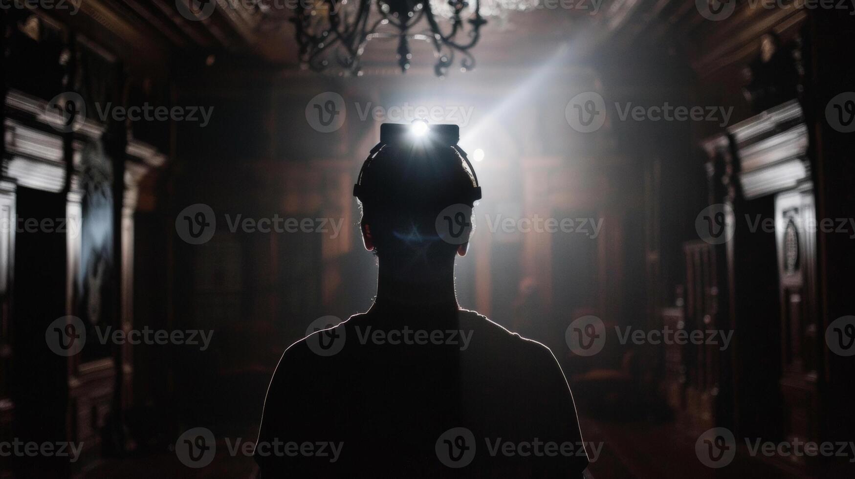 A person wearing a headlamp stands with back to the camera silhouette illuminated against the dark and foreboding interior . photo