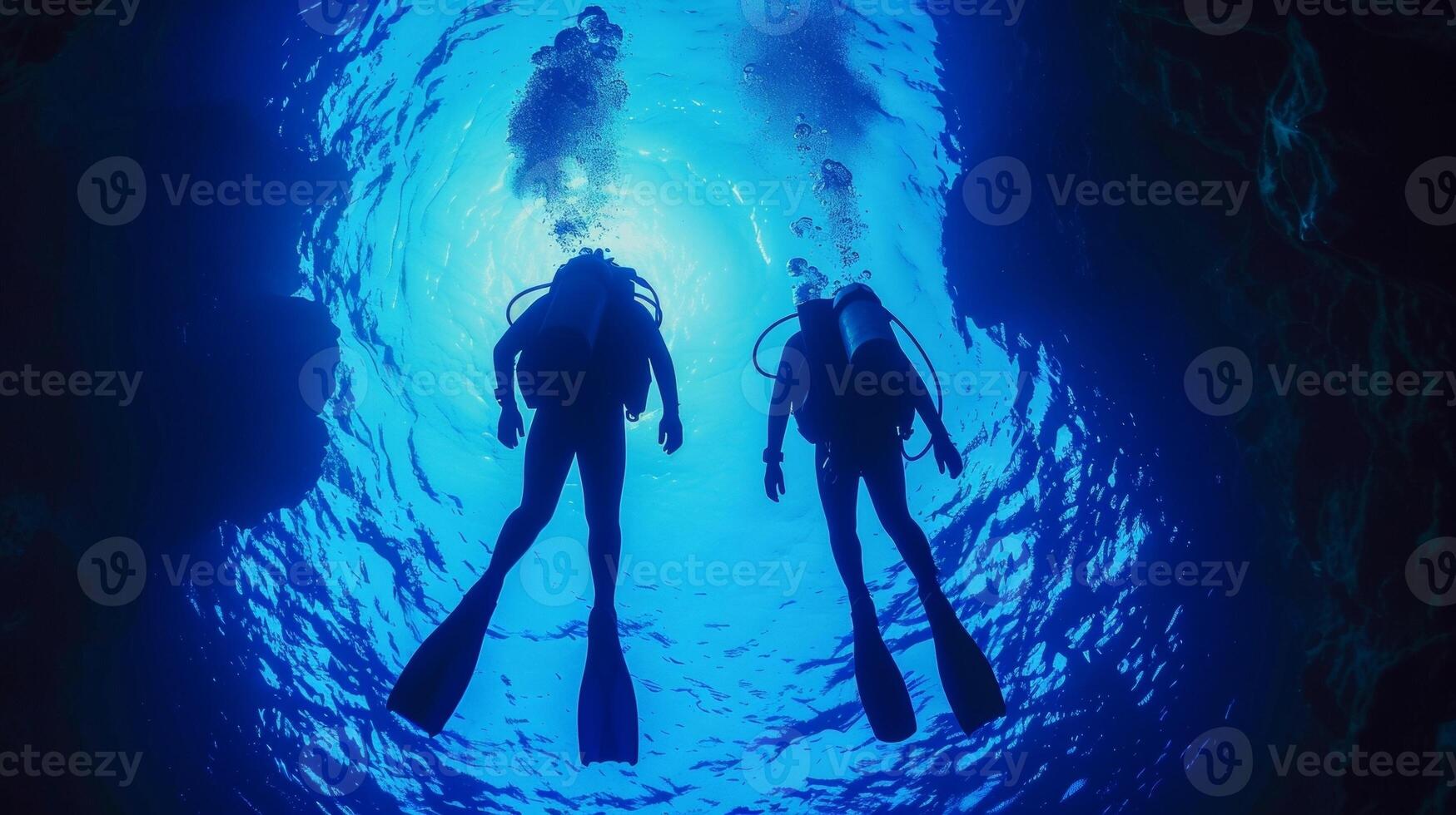 Two divers in full scuba gear cautiously make way towards the vortex silhouettes against the vibrant blue hues of the . photo