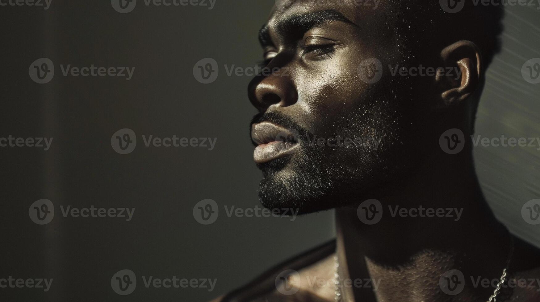 Against a backdrop of dark shadows a confident black man stands tall with his head held high. The interplay of light and shadows on his chiseled features highlights his refined sense photo