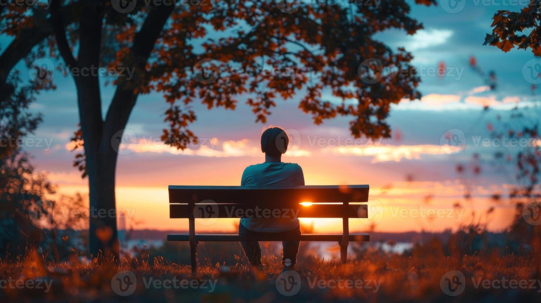 A person sitting on a park bench watching the sunset and admiring the colors without trying to capture it on their phone photo