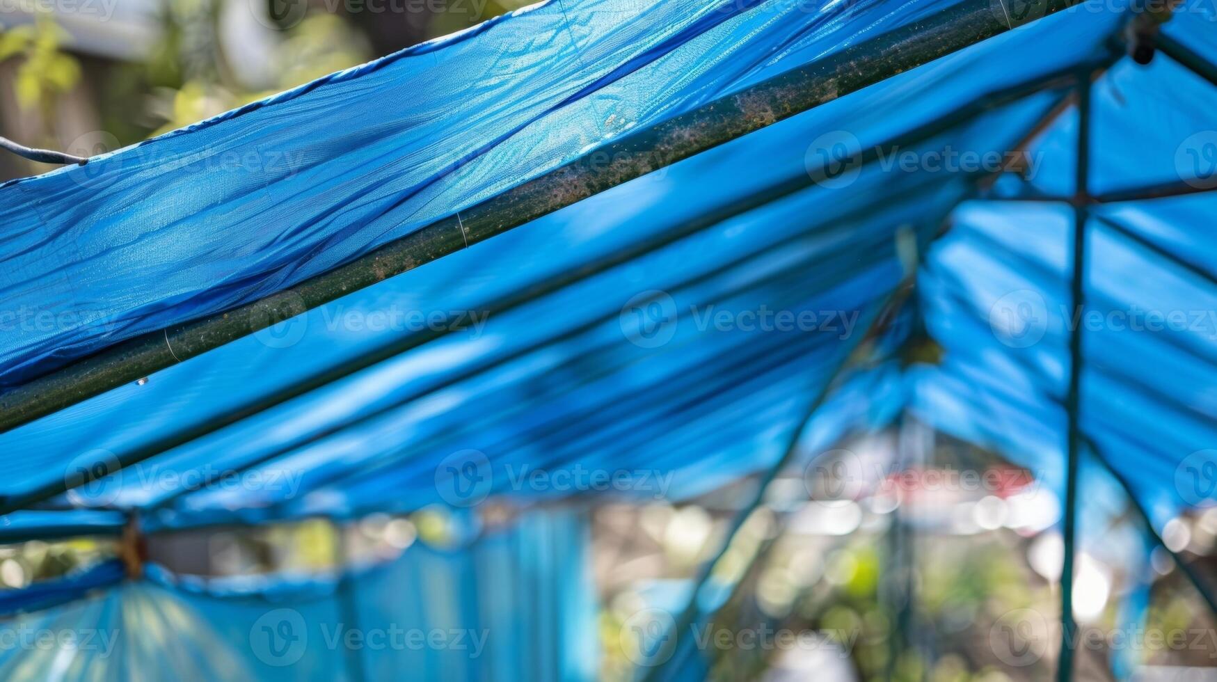 A blue plastic tarp is carefully dd over a large metal frame creating a makeshift roof for a makeshift rainwater harvesting system in an open space photo