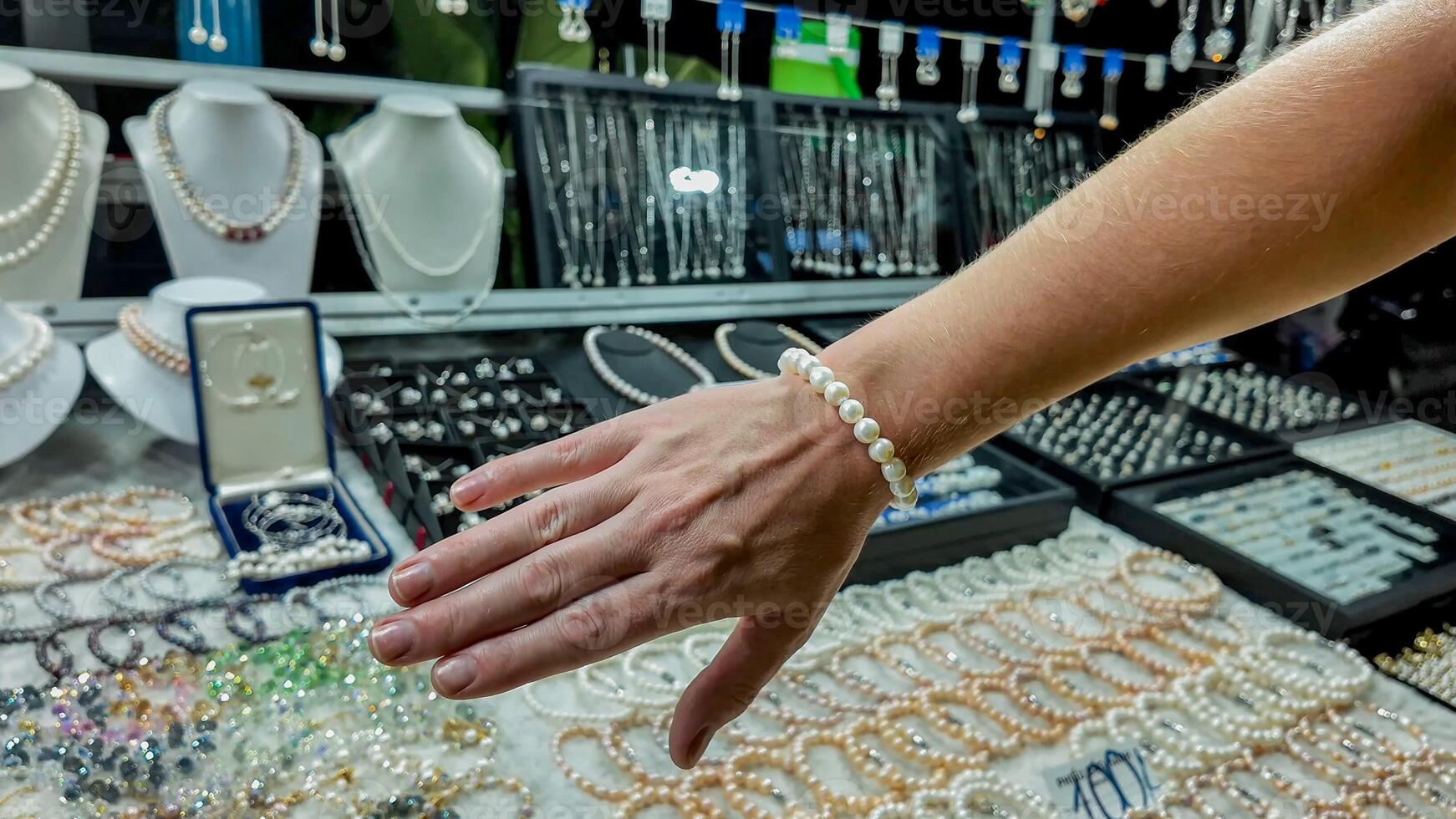 Womans hand adorned with pearl bracelet over a display of various jewelry, concept for luxury shopping or Valentines Day gift selection photo