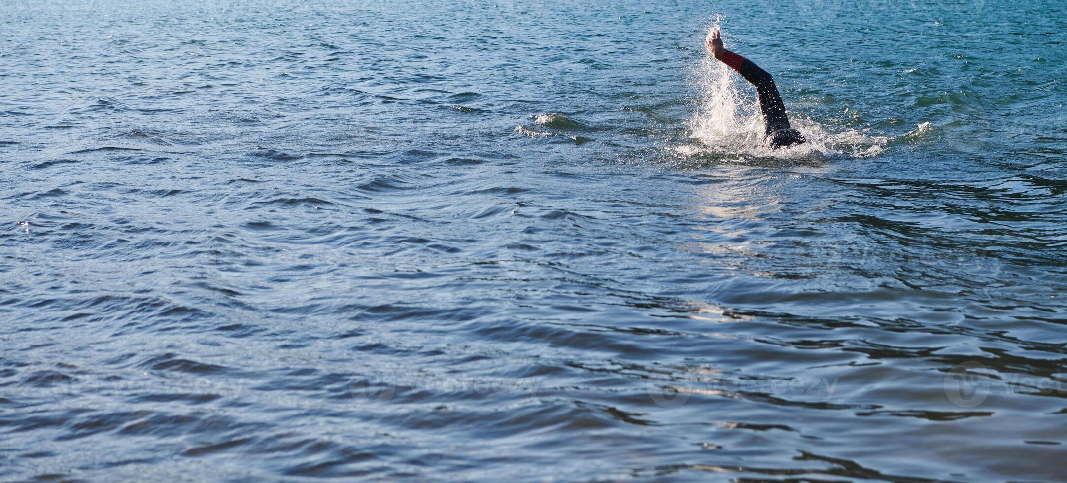 Triathlon athlete swimming on lake in sunrise wearing wetsuit photo