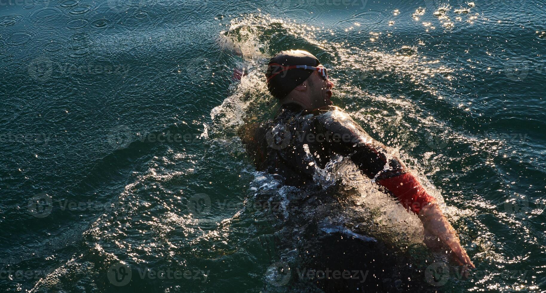 Triathlon athlete swimming on lake in sunrise wearing wetsuit photo