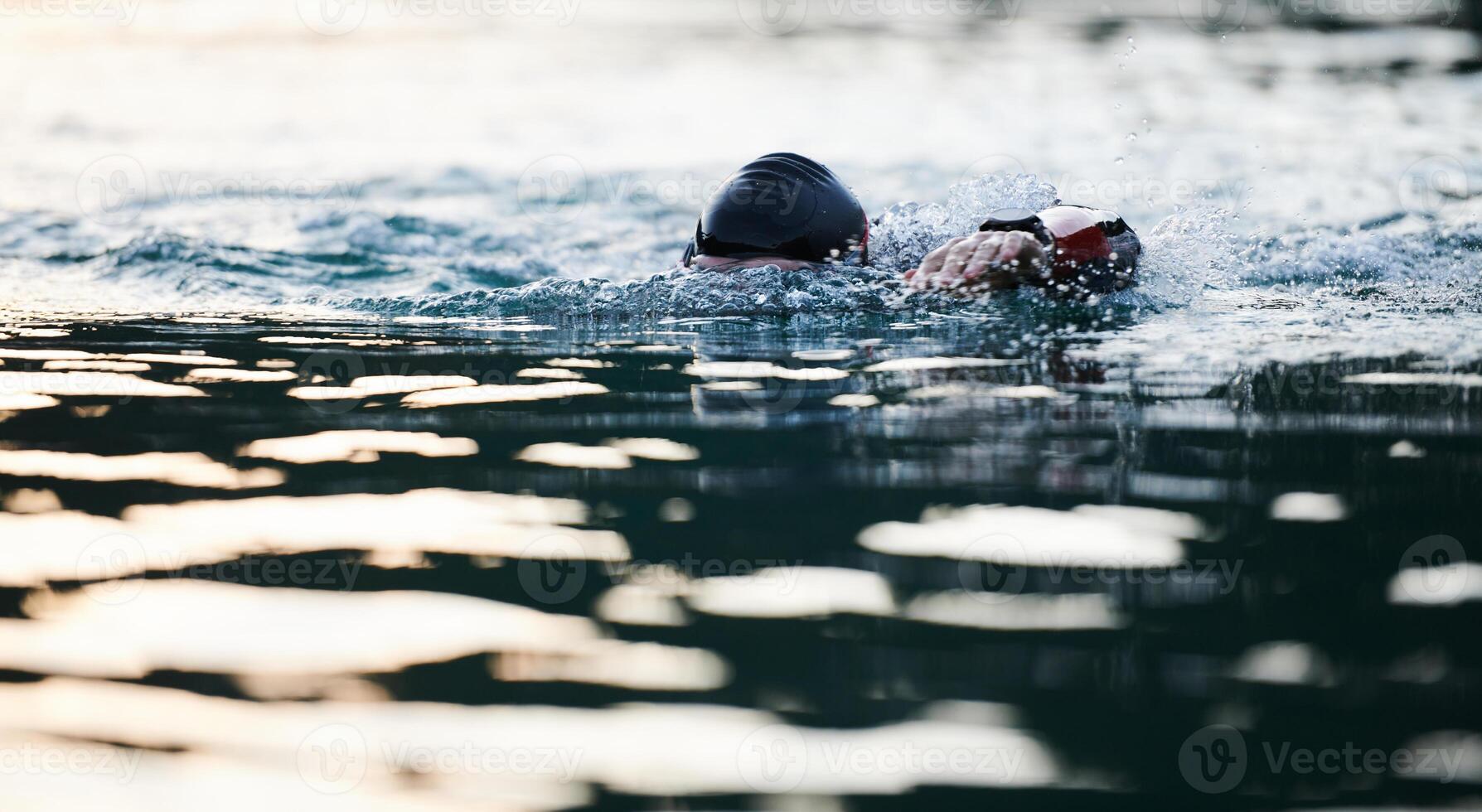 Triathlon athlete swimming on lake in sunrise wearing wetsuit photo