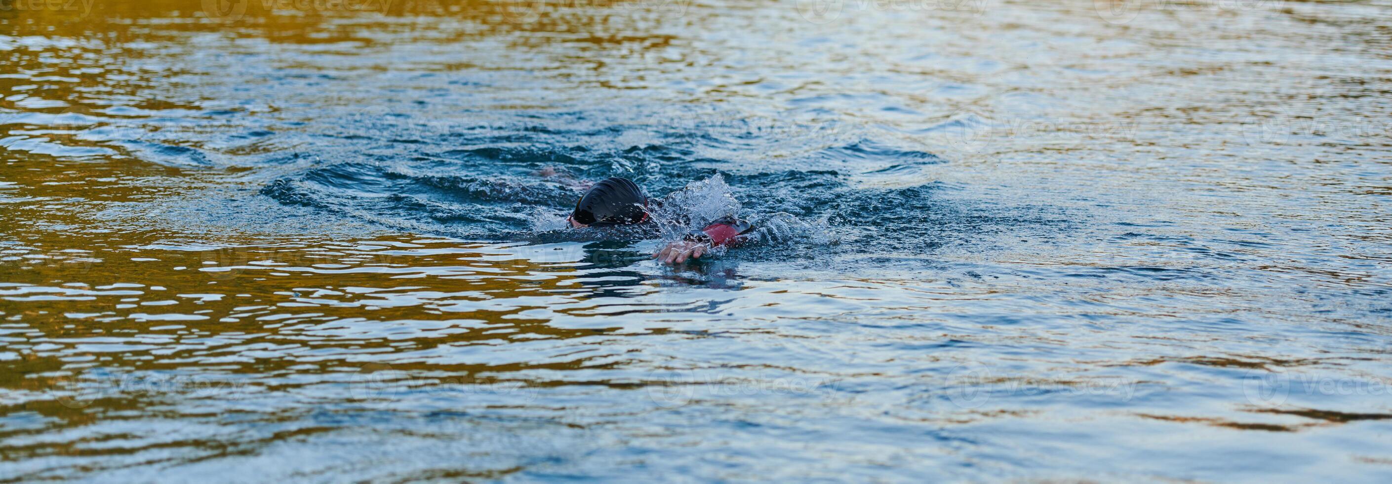 Triathlon athlete swimming on lake in sunrise wearing wetsuit photo
