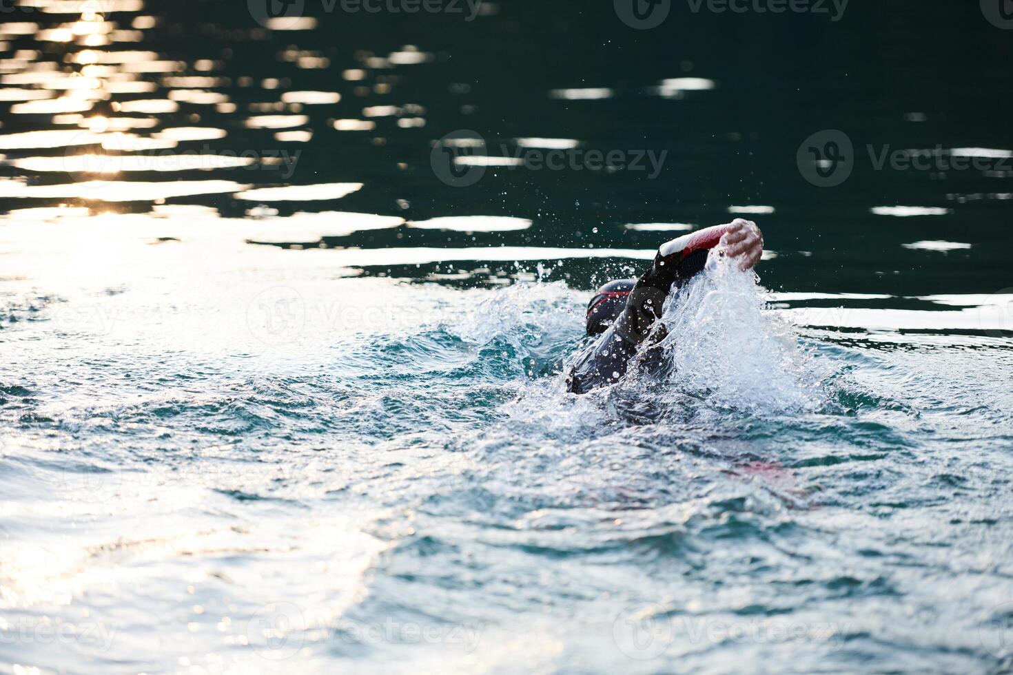 Triathlon athlete swimming on lake in sunrise wearing wetsuit photo