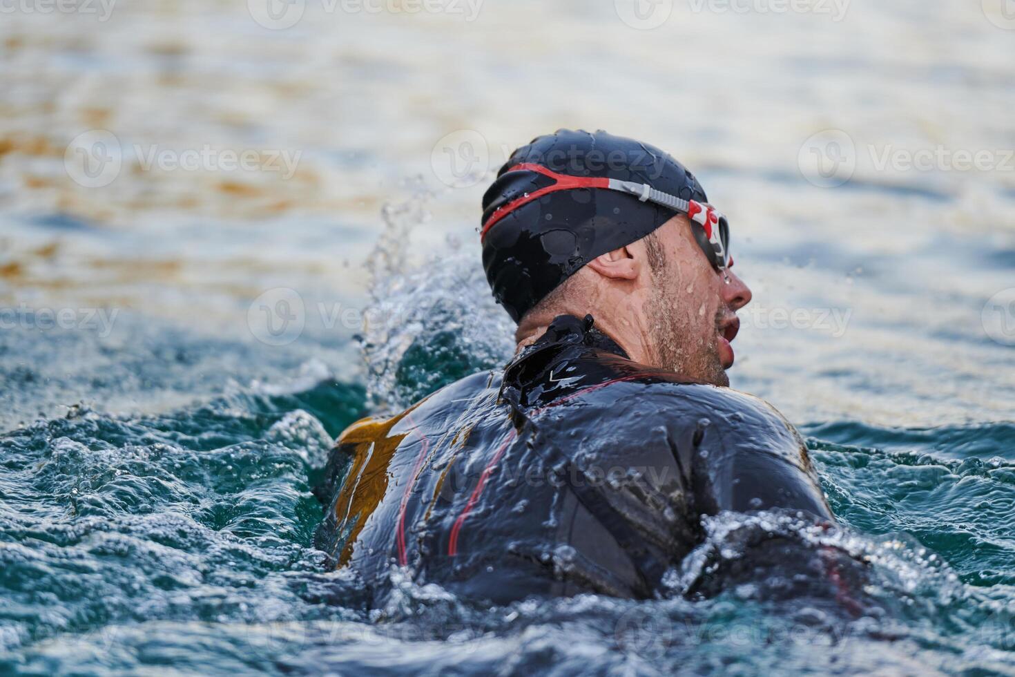 Triathlon athlete swimming on lake in sunrise wearing wetsuit photo
