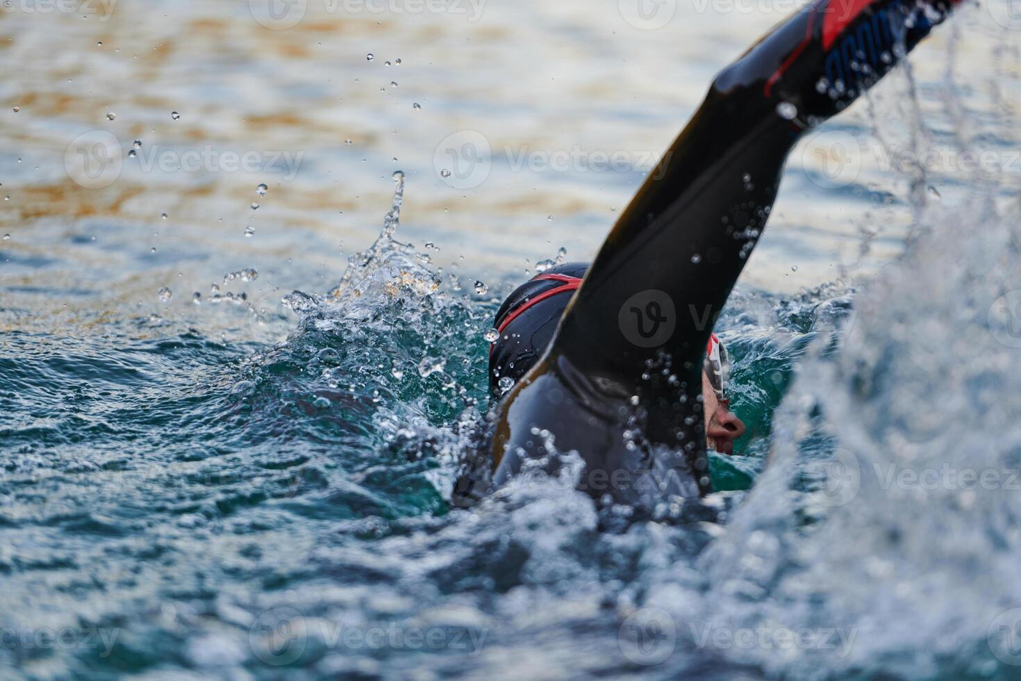 Triathlon athlete swimming on lake in sunrise wearing wetsuit photo