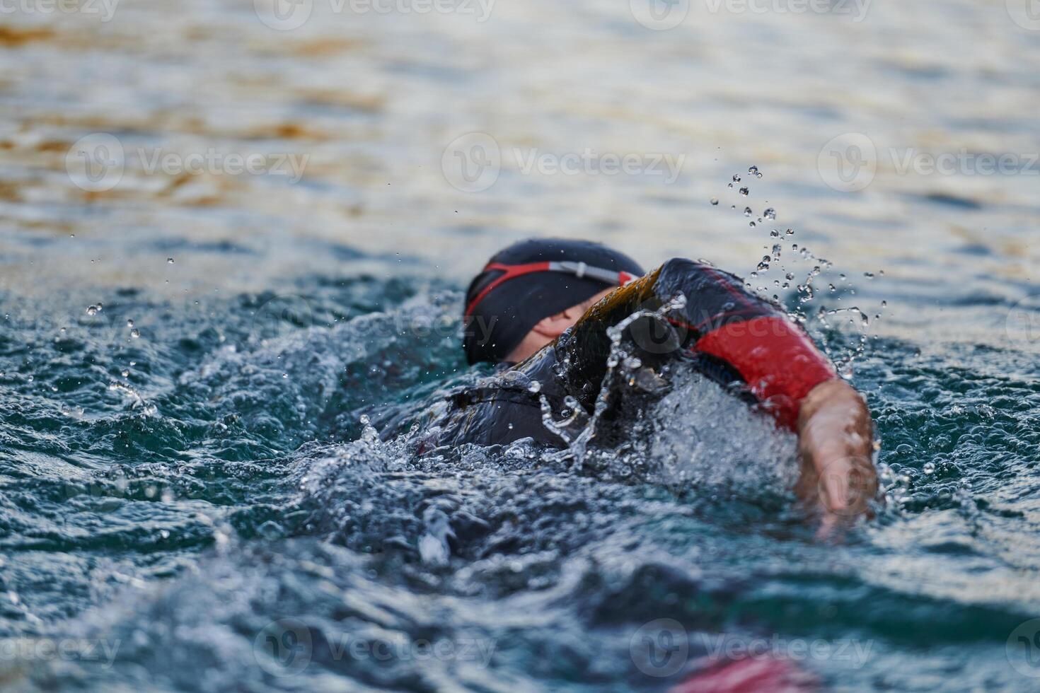 Triathlon athlete swimming on lake in sunrise wearing wetsuit photo