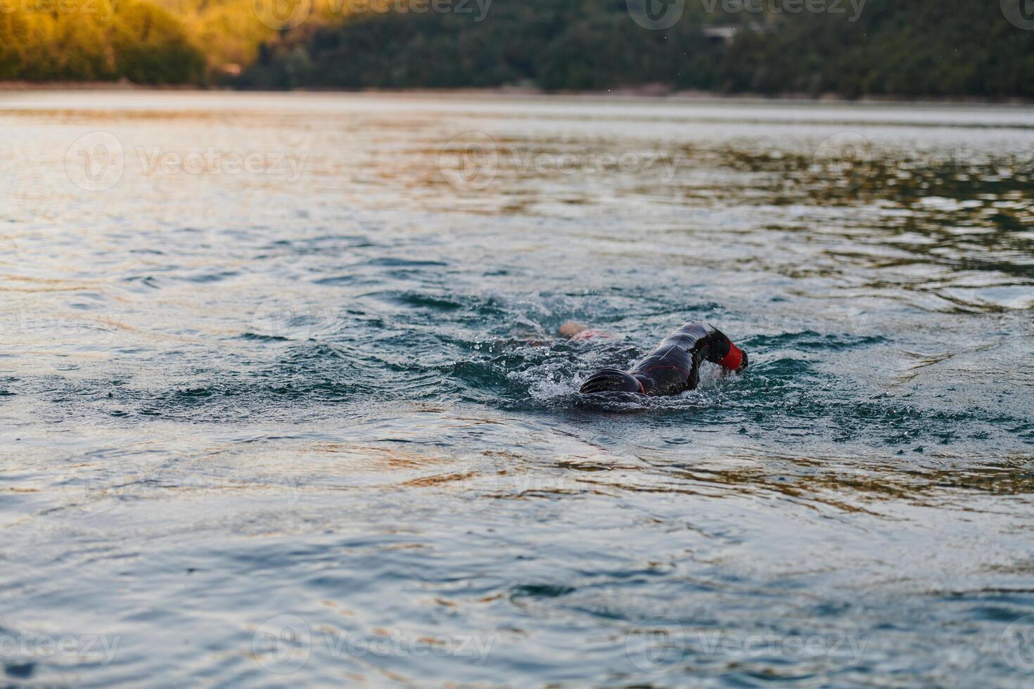 Triathlon athlete swimming on lake in sunrise wearing wetsuit photo