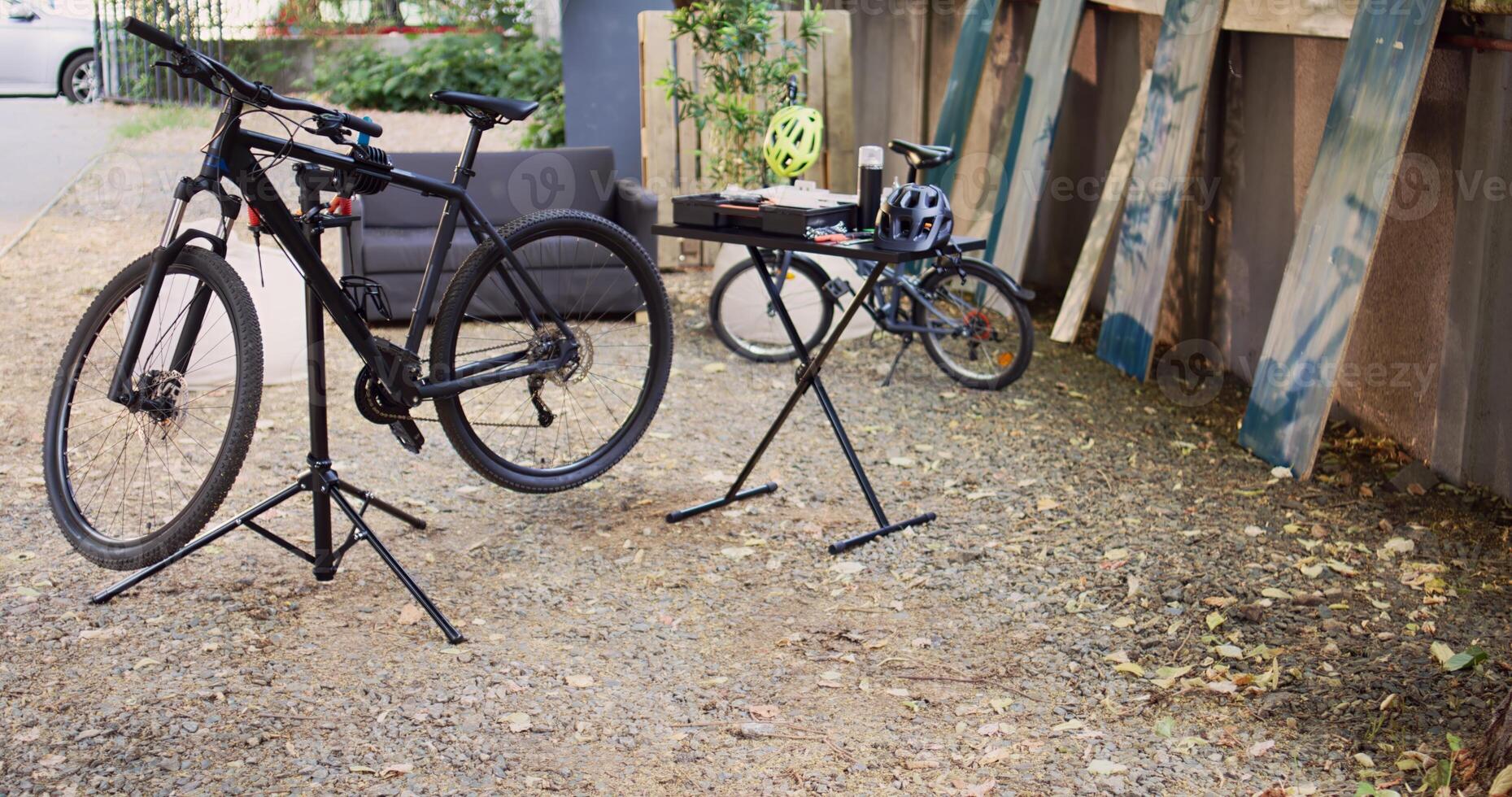 View of modern damaged bikes placed and secured in home yard ready for maintenance with professional equipment. Aerial shot of bicycle on repair-stand next to specialized toolbox outdoor. photo