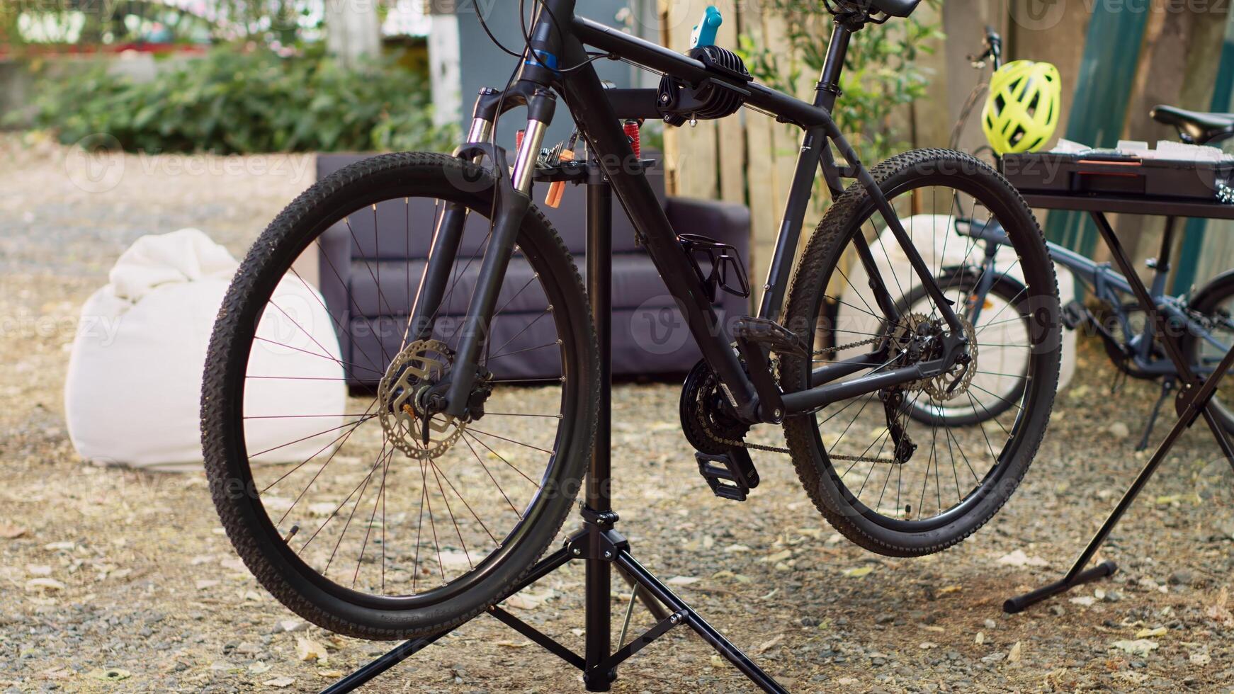 Modern bicycle is visible in the yard positioned on repair-stand for examining and mending. Outdoor various bike components await adjustments and restoration with professional work tools. photo